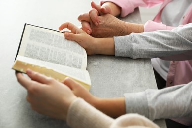 Photo of Boy and his godparents reading Bible together at grey table, closeup