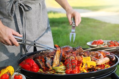Image of Man cooking meat and vegetables on barbecue grill in park, closeup