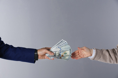 Man giving bribe money to woman on grey background, closeup