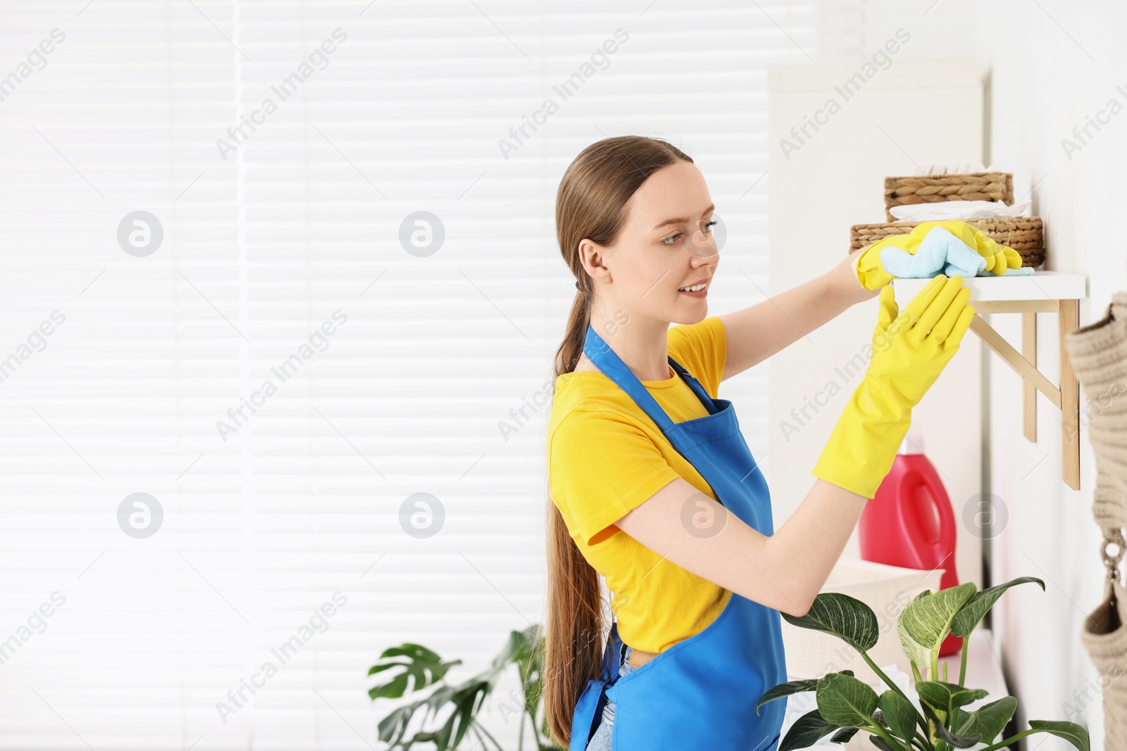 Photo of Woman cleaning shelf with rag at home, space for text
