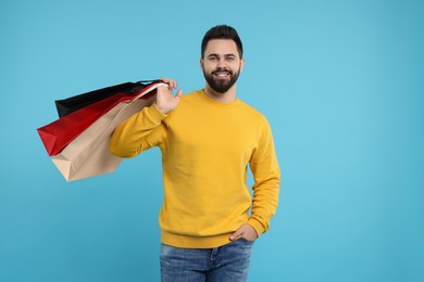 Smiling man with paper shopping bags on light blue background