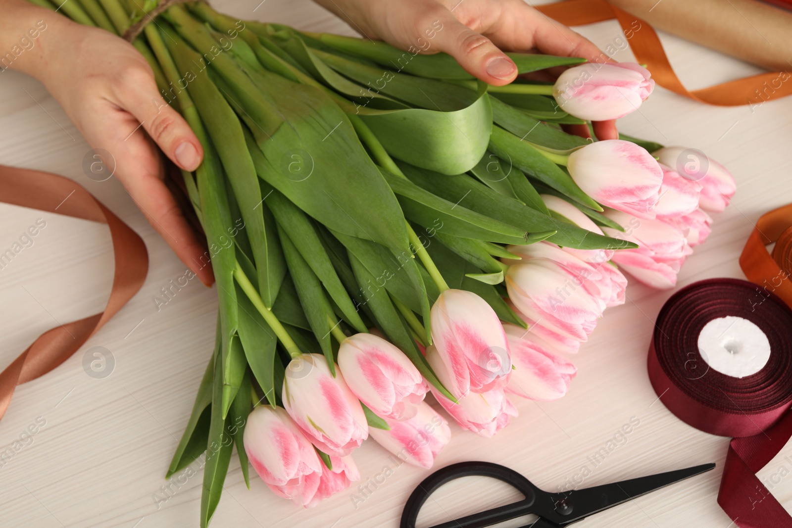 Photo of Woman making bouquet of beautiful fresh tulips at white wooden table, closeup