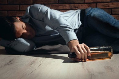 Photo of Addicted man with glass bottle of alcoholic drink lying on floor near red brick wall