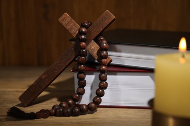 Bible, cross, rosary beads and church candle on wooden table