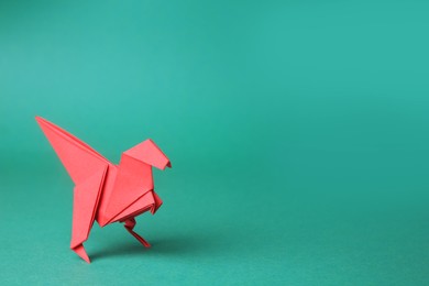 Photo of Origami art. Handmade red paper dinosaur on turquoise background, space for text