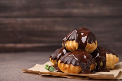 Delicious profiteroles with chocolate spread and mint on textured table, closeup. Space for text