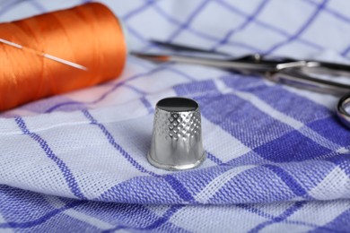 Photo of Silver thimble on checkered fabric. Sewing accessories
