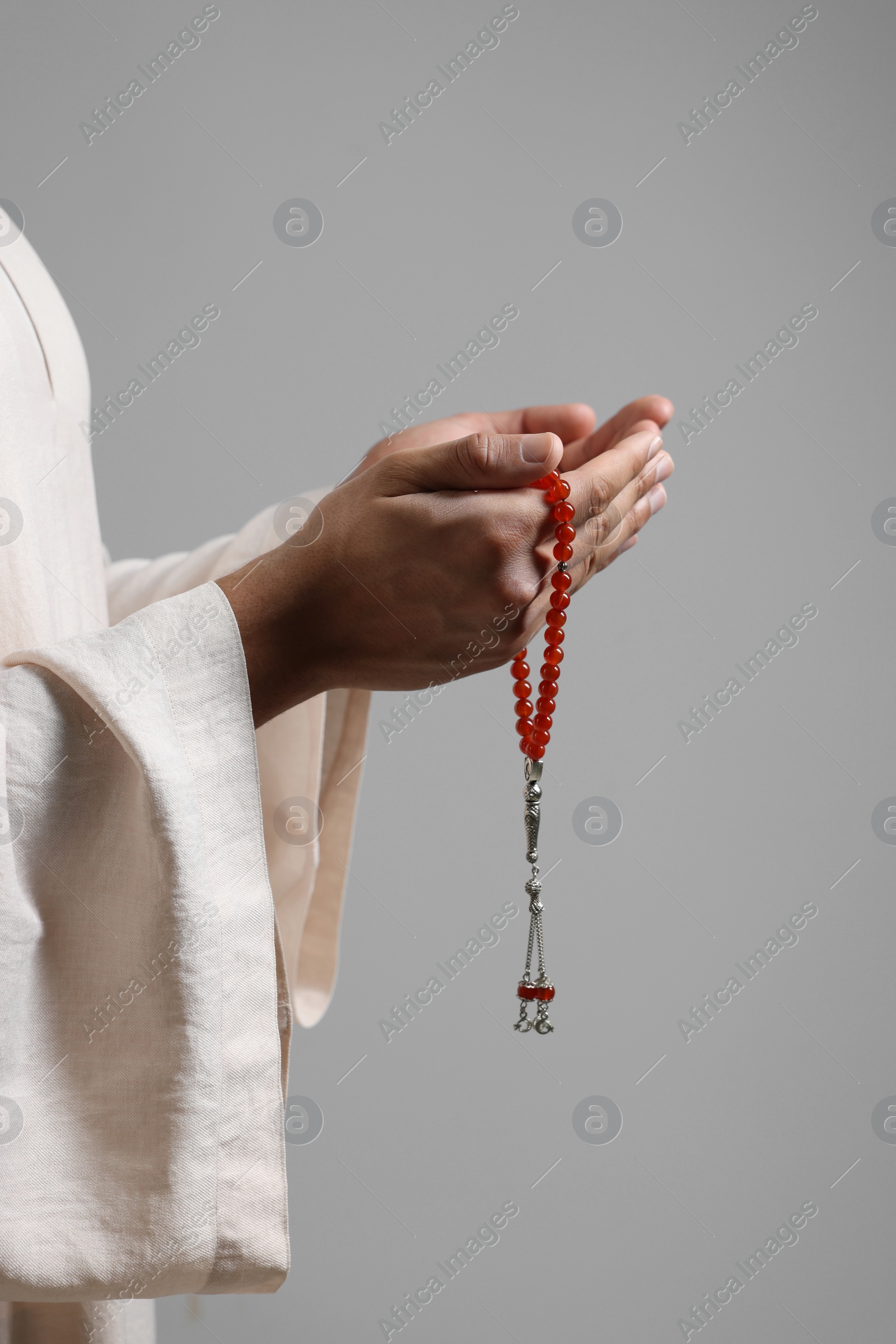 Photo of Muslim man with misbaha praying on light grey background, closeup