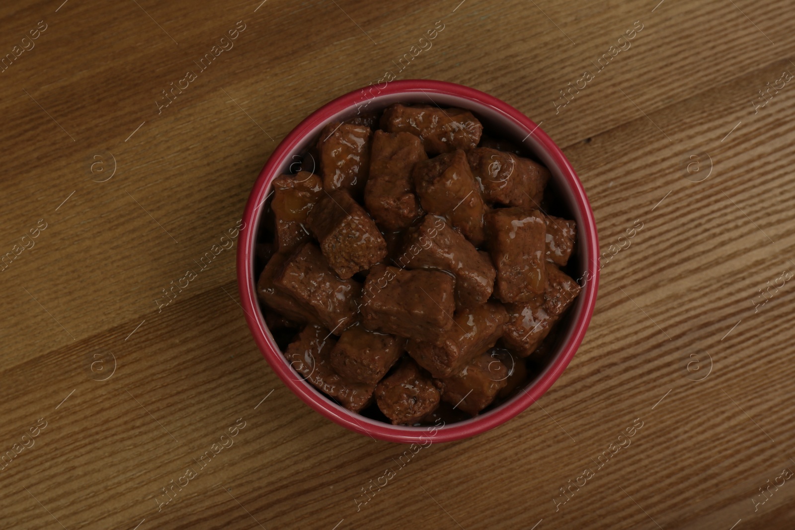 Photo of Wet pet food in feeding bowl on wooden background, top view