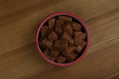 Photo of Wet pet food in feeding bowl on wooden background, top view