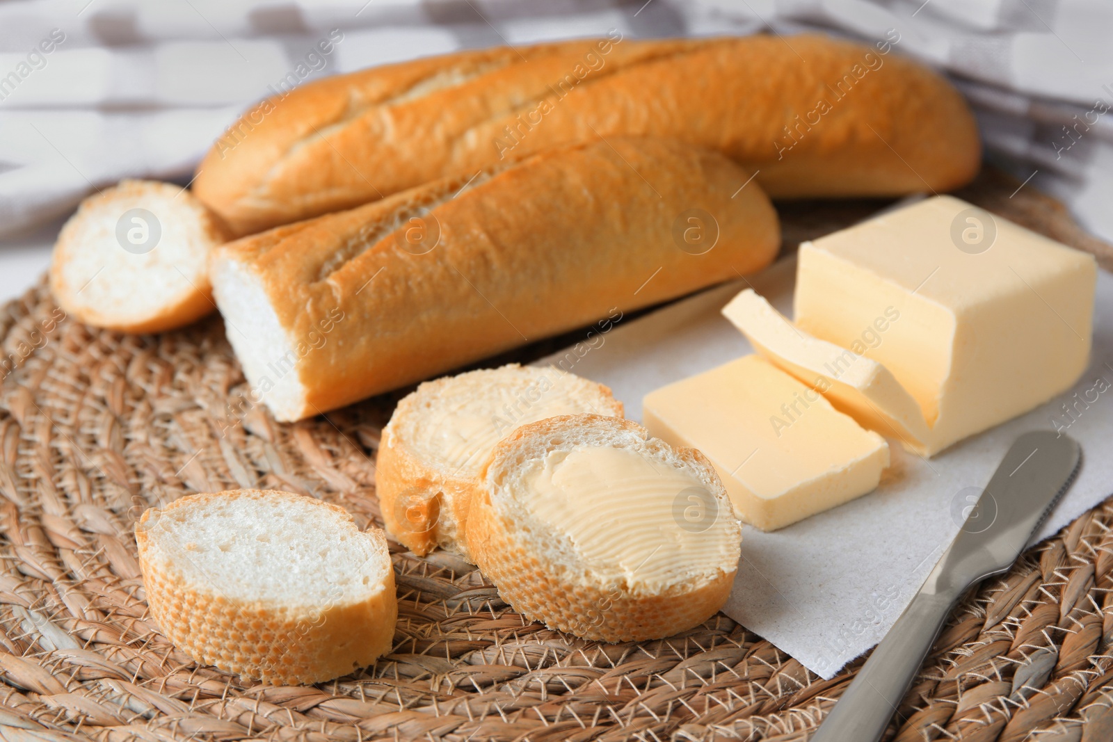 Photo of Tasty cut baguette with fresh butter on wicker mat