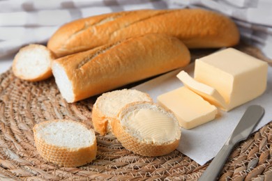 Photo of Tasty cut baguette with fresh butter on wicker mat