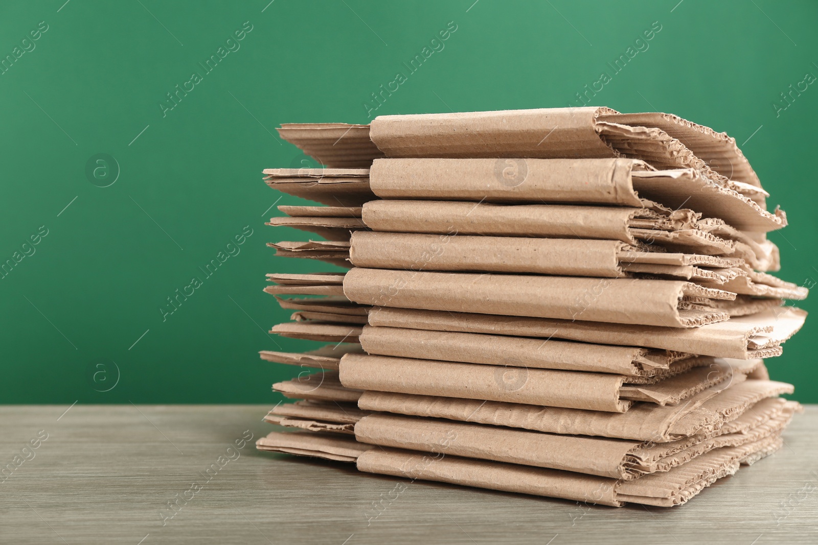 Photo of Cardboard pile on table against color background, space for text. Waste recycling concept