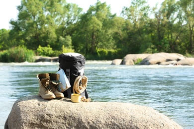 Photo of Backpack and camping equipment on rock near river. Space for text