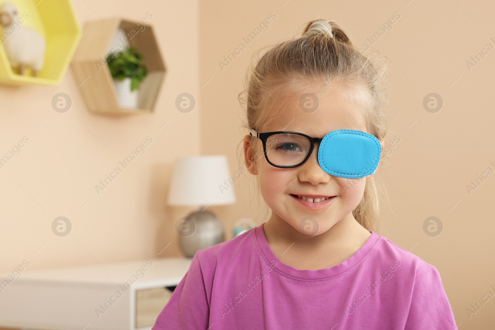 Photo of Girl with eye patch on glasses in room, space for text. Strabismus treatment