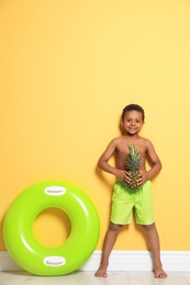 Photo of Cute African American boy with pineapple and bright inflatable ring near color wall