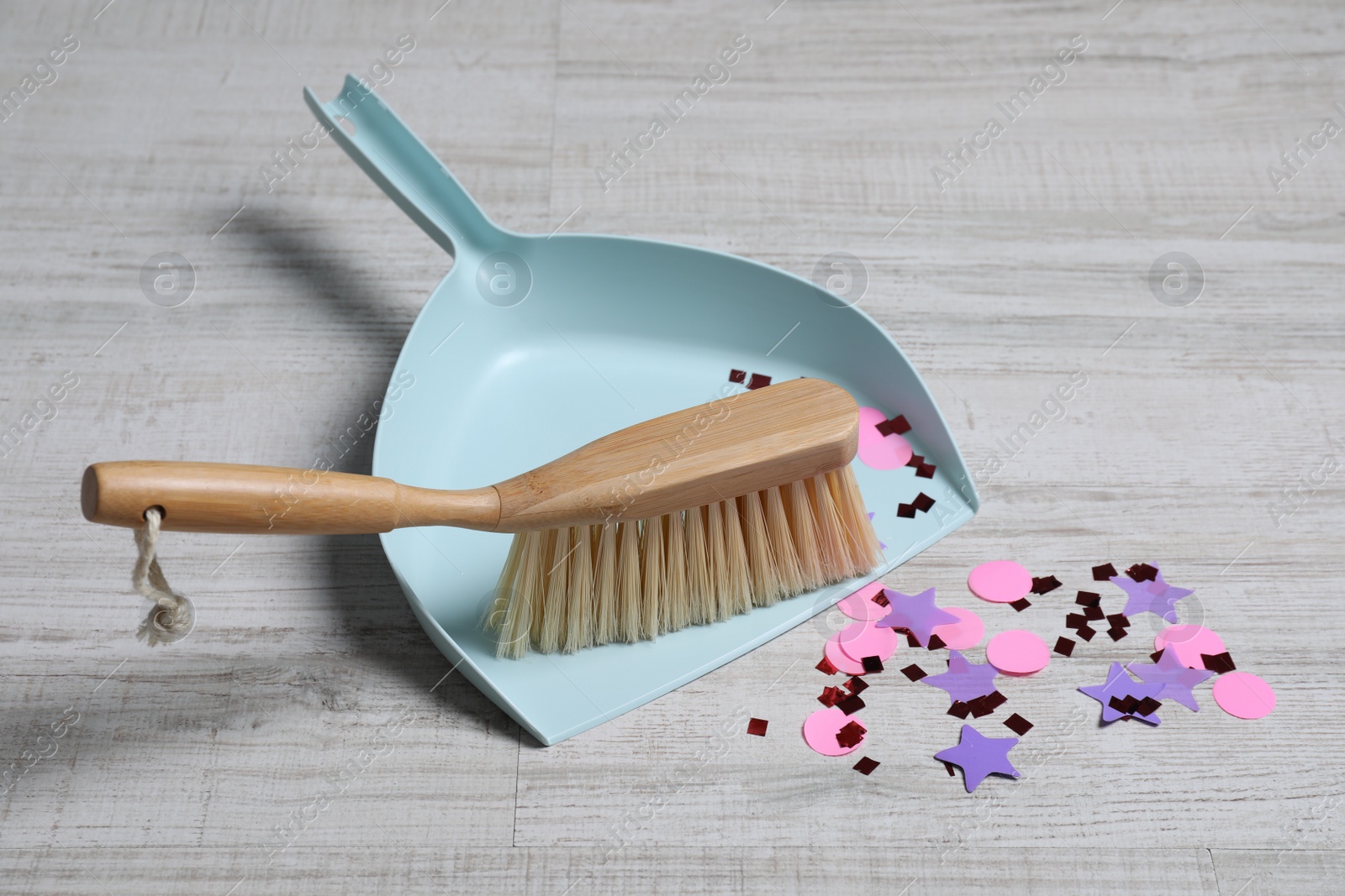 Photo of Light blue dustpan, wooden brush and bright confetti on floor