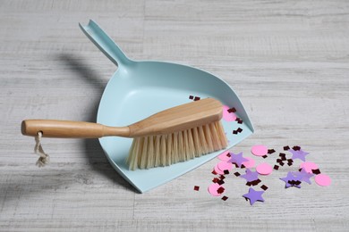 Light blue dustpan, wooden brush and bright confetti on floor