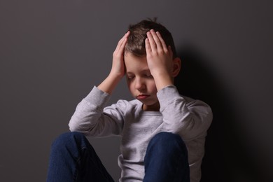 Photo of Child abuse. Upset boy near gray wall