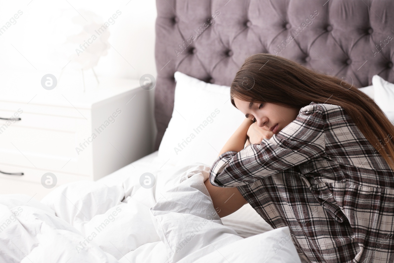 Photo of Upset teenage girl sitting on bed. Space for text