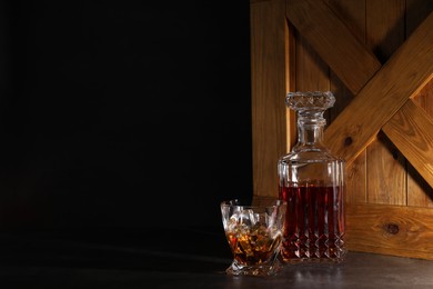 Whiskey in glass and bottle near wooden crate on dark table against black background. Space for text