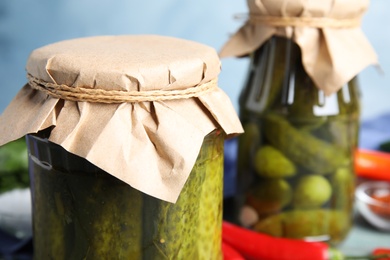 Photo of Jars with pickled cucumbers on blue background, closeup view