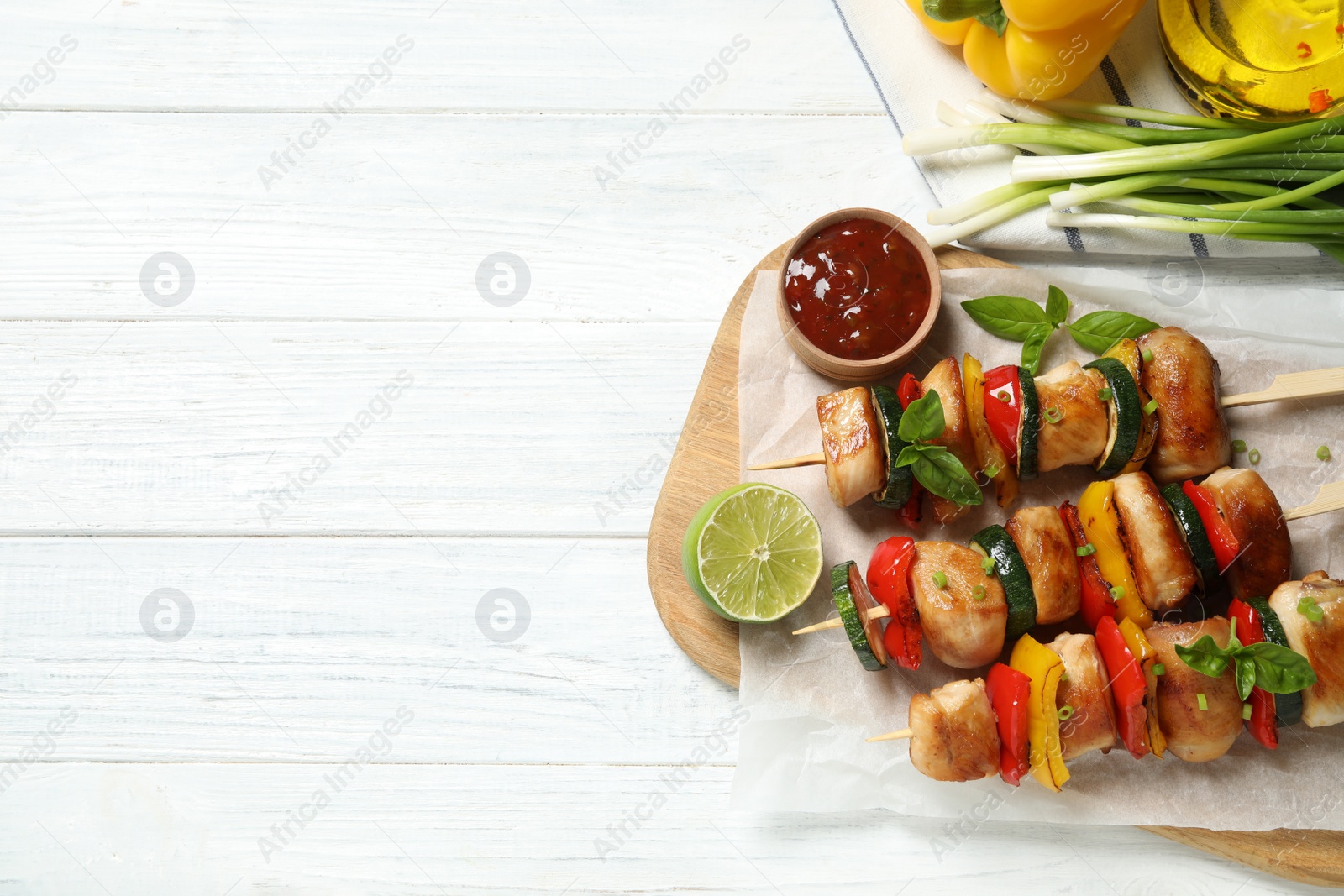 Photo of Delicious chicken shish kebabs with vegetables and ketchup on white wooden table, flat lay. Space for text