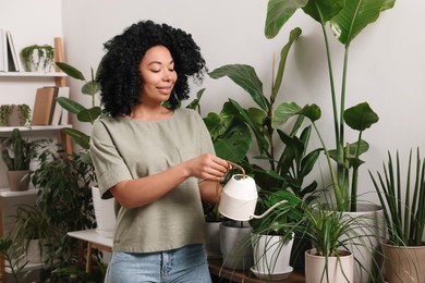 Photo of Happy woman watering beautiful potted houseplants at home