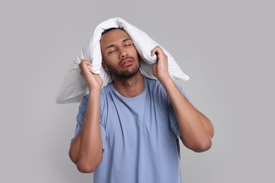 Photo of Tired man covering ears with pillow on light grey background. Insomnia problem