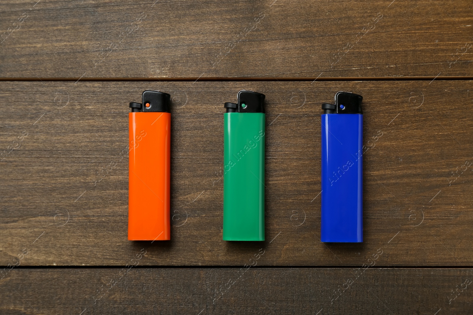 Photo of Colorful plastic cigarette lighters on wooden table, flat lay