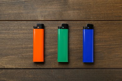 Colorful plastic cigarette lighters on wooden table, flat lay