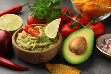 Bowl of delicious guacamole, nachos chips and ingredients on grey table, closeup