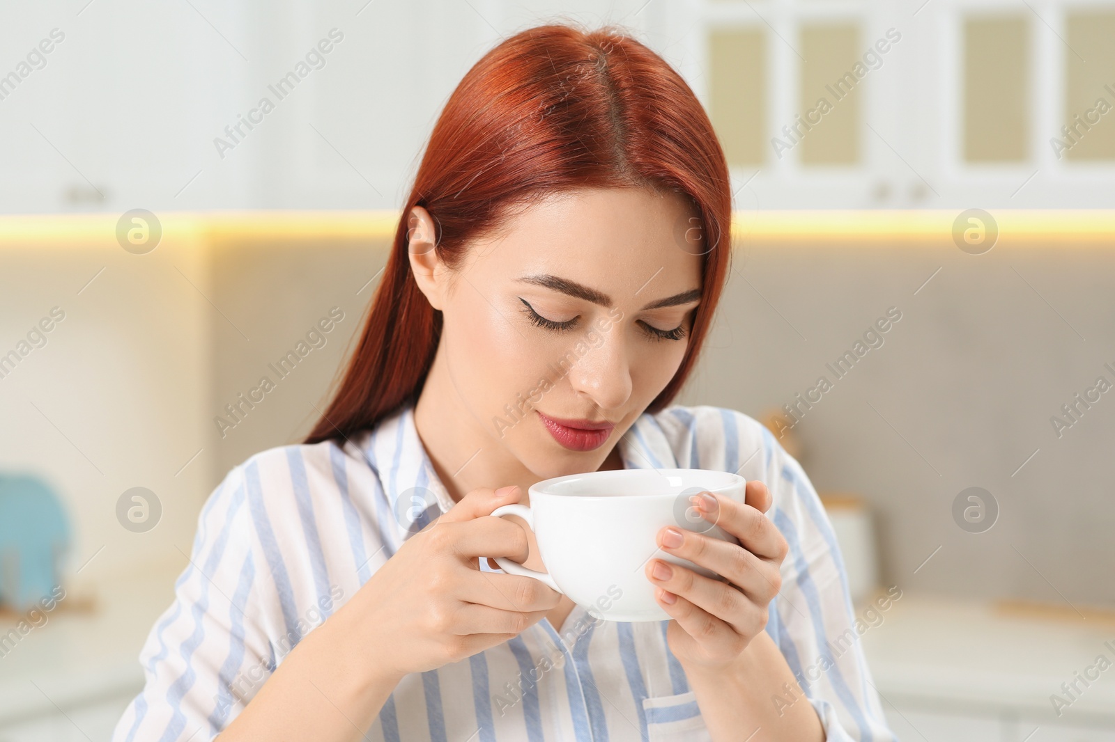 Photo of Beautiful woman with red dyed hair enjoying cup of drink in kitchen