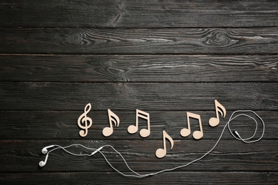 Photo of Flat lay composition with music notes, earphones and space for text on wooden background