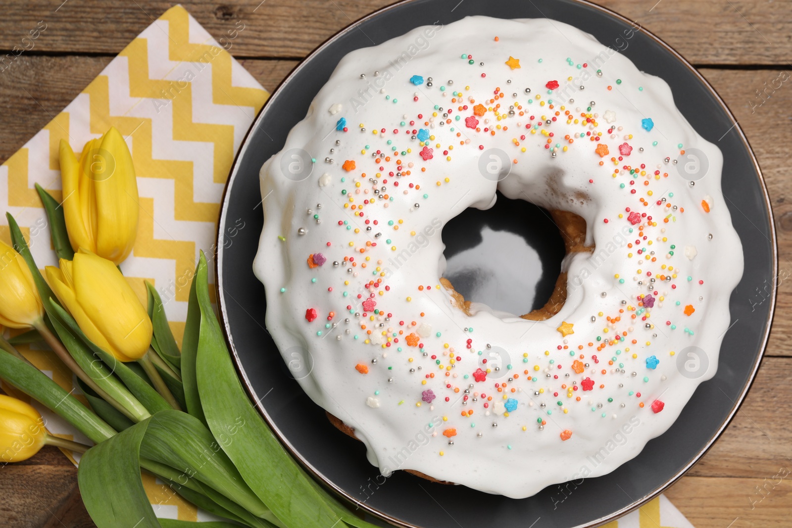 Photo of Easter cake with sprinkles and tulips on wooden table, flat lay