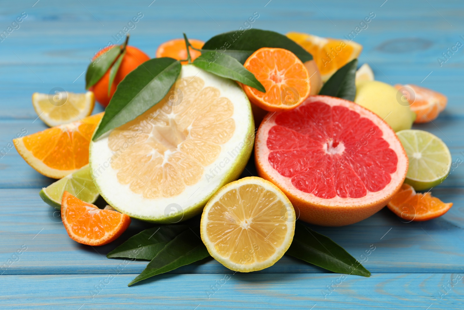 Photo of Different citrus fruits with fresh leaves on light blue wooden table