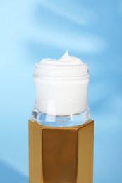 Photo of Open jar of cream on display against blue background