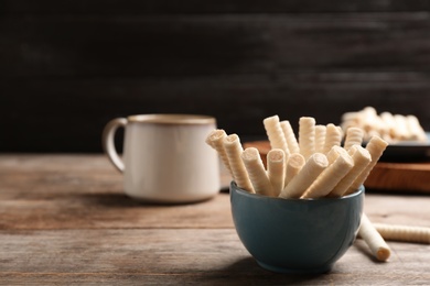 Bowl with delicious wafer rolls on wooden table, space for text. Sweet food