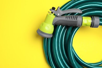 Watering hose with sprinkler on yellow background, top view. Space for text
