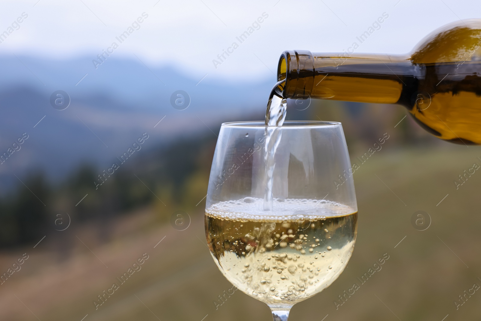Photo of Pouring white wine into glass in mountains, closeup