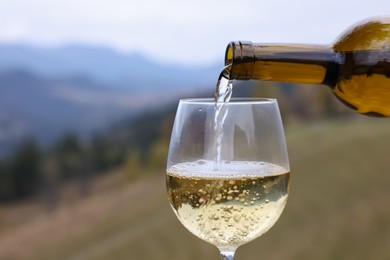 Photo of Pouring white wine into glass in mountains, closeup