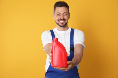 Photo of Man showing motor oil against orange background, focus on container