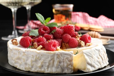 Photo of Brie cheese served with raspberries and walnuts on black plate, closeup