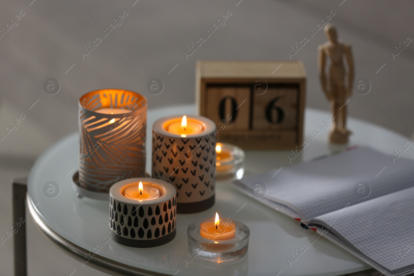 Photo of Burning candles in holders and notebook on white table indoors