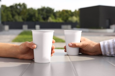 Photo of Coffee to go. Couple with paper cups at table outdoors, selective focus