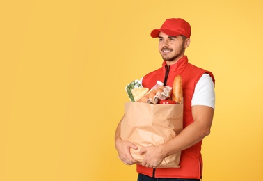 Food delivery courier holding paper bag with products on color background. Space for text