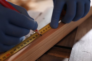 Photo of Professional carpenter making mark on wooden bar in workshop, closeup