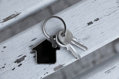 Keys with trinket in shape of house on wooden surface, top view. Real estate agent services