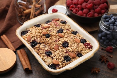 Photo of Tasty baked oatmeal with berries, almonds and spices in baking tray on wooden table, closeup