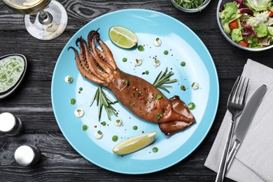 Photo of Delicious grilled squid served on black wooden table, flat lay